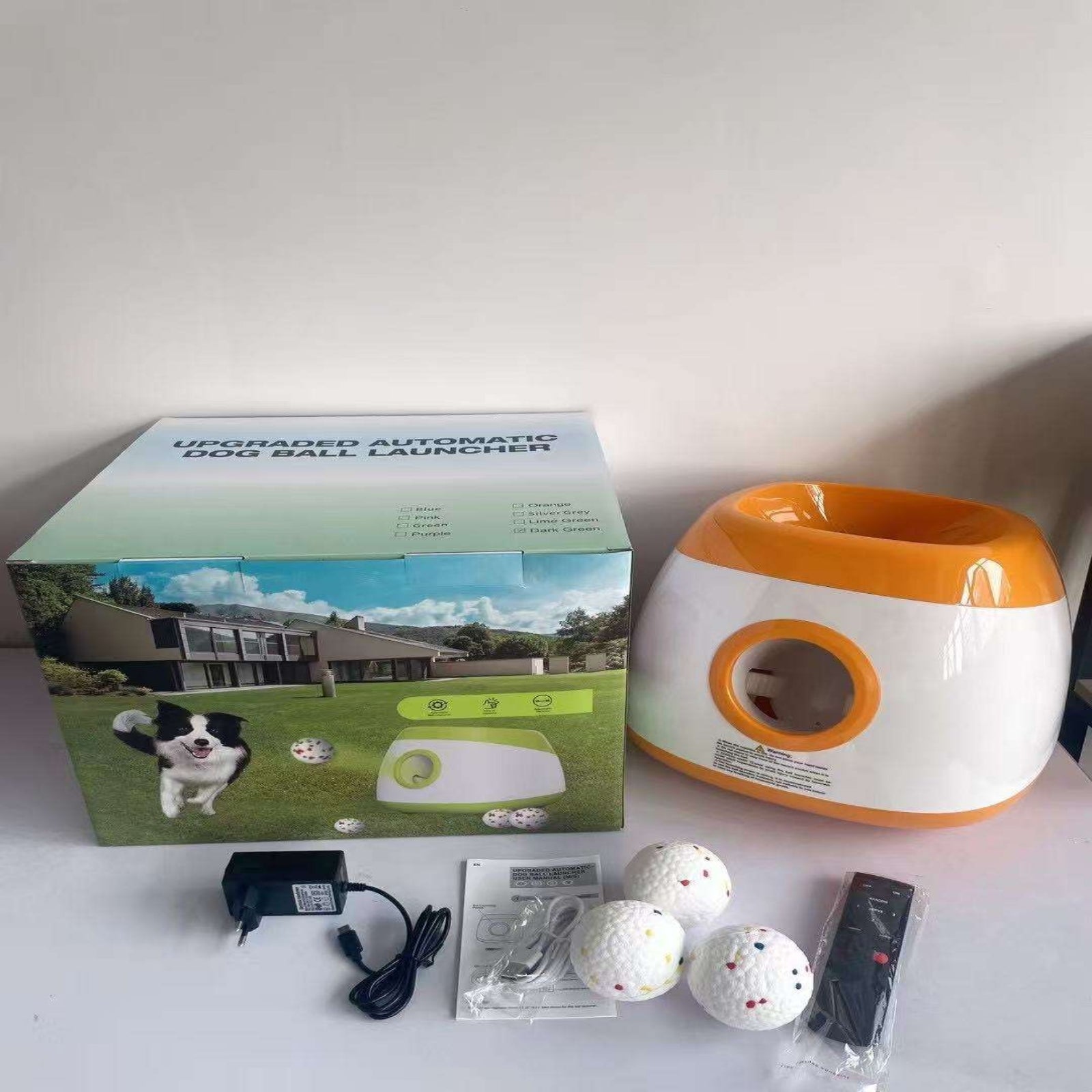 Dog ball launcher with packaging, remote control, and balls on a white surface